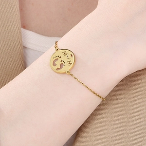 Detail of gold chain bracelet featuring a round MOM charm with baby footprints on wrist