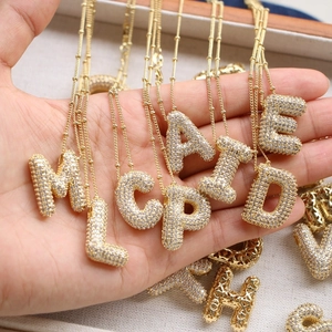 Gold bubble letter necklace with cubic zirconia paving in a hand-held display