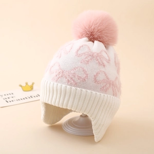 Detail of knit earflap hat showing bow jacquard pattern and soft pink pompom ball