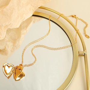 Elegant gold heart locket necklace with fine chain displayed on a mirror surface
