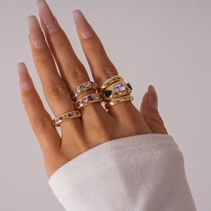 Close-up of six gold rings set with pink and purple gemstones on a model hand