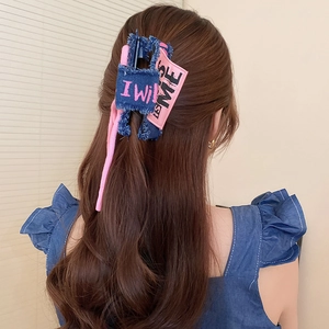 Detail of pink and blue denim bow hair claw clip worn by a model on light background