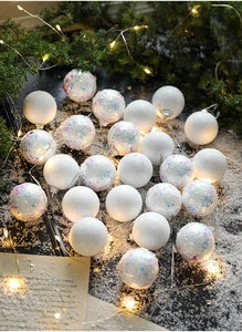 Close-up of matte white and glitter Christmas balls with festive pine and warm lights