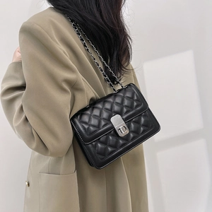 Detail of a black quilted crossbody bag with silver chain strap worn by a model