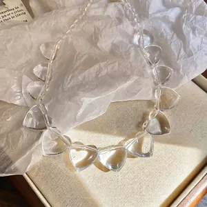Minimalist irregular clear acrylic heart bead choker necklace on white textured background