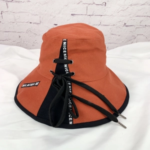 Gros plan du chapeau bob orange avec laçage noir et ruban décoratif lettré