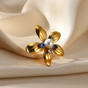Close-up of golden flower ring with white pearl center and blue gemstone accents