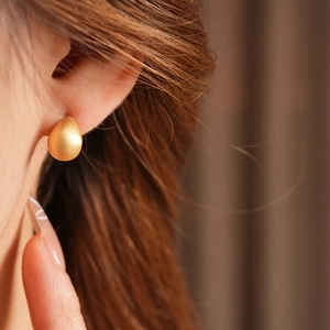 Close-up of minimalist gold plated teardrop earrings on model with brushed metal finish