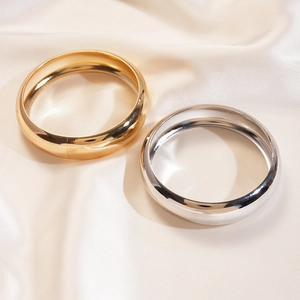 Detail of polished gold and silver thick bangles on soft beige silk background