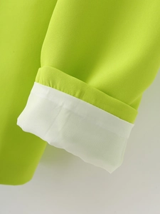 Détail du poignet du blazer vert vif montrant la texture du tissu et la doublure blanche