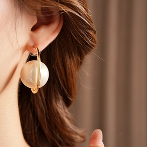 Close-up of a model wearing gold C-shaped earrings with a large white pearl bead