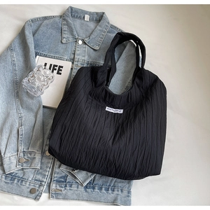Detail der schwarzen Plissee-Einkaufstasche mit Kiss Yourself Etikett auf Denim-Hintergrund