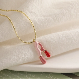 Détail d'un collier doré avec pendentif lettre A émaillé rose et rouge sur tissu blanc