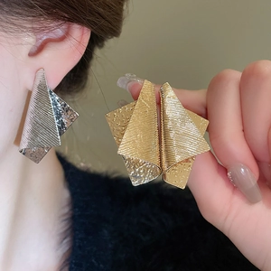 Macro view of geometric folded metal earrings with textured brushed and hammered surface