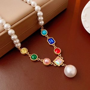 Close-up of pearl necklace with colorful gemstones and large drop pearl on a jewelry box