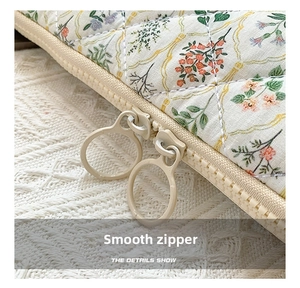 Detail of floral quilted laptop sleeve showing smooth dual zippers and round metal pulls