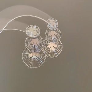 Détail de boucles d'oreilles à triple cercle argenté avec motifs radiaux ajourés