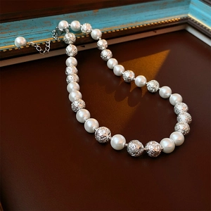 Vue macro d'un collier vintage français avec perles blanches et billes en métal argenté