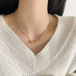 Nahaufnahme der goldenen Perlenhalskette an einem Model im weißen Strickpullover