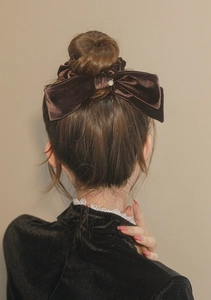 Close-up of a large dark brown velvet bow scrunchie with a gold metal tag on hair