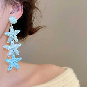 Detail showing blue raffia star tassel earrings with woven texture on model