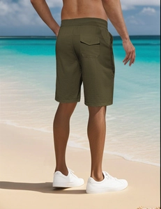 Men's olive green sports shorts with elastic waist and back pocket shown on beach