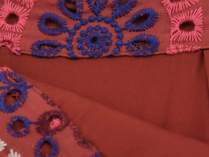 Detail der floralen Hohlstickerei und Nahtdetails auf rostrotem Stoffgewebe