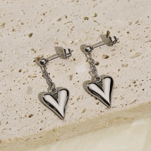 Polished silver heart drop earrings with chains on textured stone background
