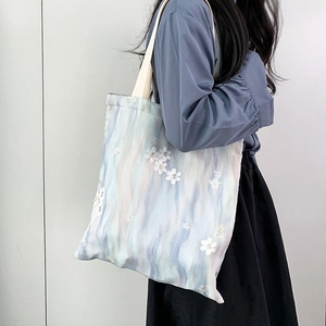 Détail de broderie florale sur un sac en toile dégradé bleu clair et rose porté par mannequin