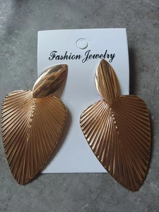 Detailed view of gold fan leaf earrings with radial texture on a jewelry display card