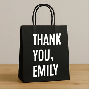 Detail of custom black gift bag with Thank You Emily text on a light wooden surface
