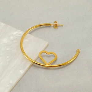 Minimalist golden hoop earring with hollow heart design on a clean textured background