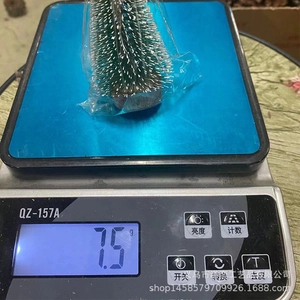 Miniature snow-dusted pine tree being weighed on a digital scale showing 7.5g total weight