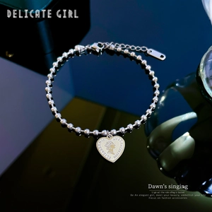 Macro detail of silver ball chain bracelet featuring a heart-shaped Elizabeth II coin pendant
