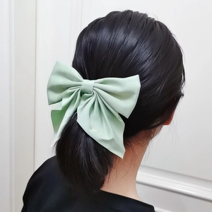 Detail of a large light green fabric bow hair clip worn as a ponytail accessory