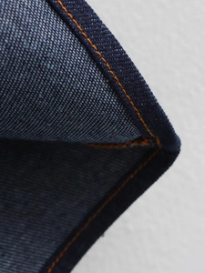 Close-up of deep blue denim fabric texture and orange double stitching detail