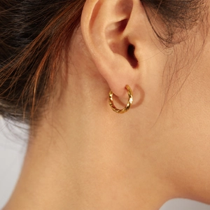 Close-up of golden mobius loop earrings with spiral twist texture worn on the ear