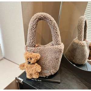 Vue détaillée du sac seau en peluche taupe avec breloque ours posé sur des livres