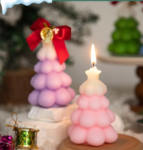 Macro shot of lit pink and purple Christmas tree candles with bow and bell decor