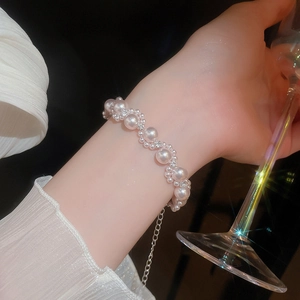 Detail of twisted pearl bracelet with rhinestones worn by a model holding a glass