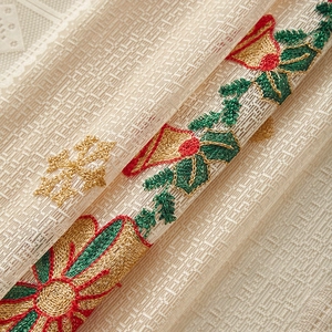 Close-up of beige lace fabric with embroidered red Christmas bells and golden snowflakes