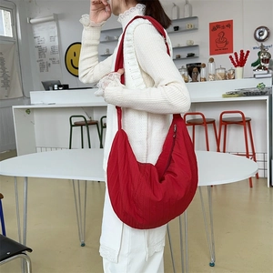 Red nylon crescent bag shown on model in a modern cafe setting with soft natural lighting