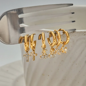 Set of gold earrings with rhinestone cross, cherry, and dog pendants on a fork