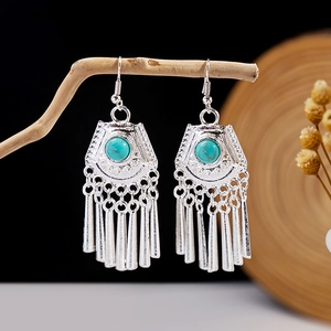 Macro detail of ethnic silver earrings with turquoise stones and bells on a wooden branch