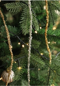 Detail of gold and silver glitter cypress leaf ornaments with warm LED lights on pine branch
