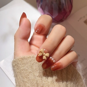 Amber gradient press-on nails with 3D bow and pearl accents on knit sweater cuff