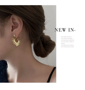 Close-up of a model wearing a golden sunburst earring with radiant polished metal lines