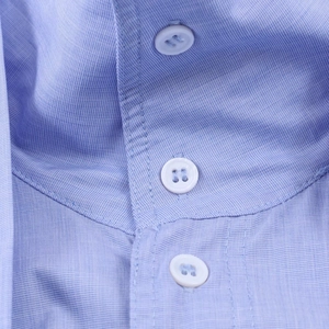 Dettaglio macro del tessuto di una camicia celeste con bottoni bianchi e cuciture