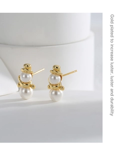 Detail of snowman earrings with gold plating and white pearl on abstract background