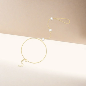Detailed view of golden hand harness with three white pearls on cream background